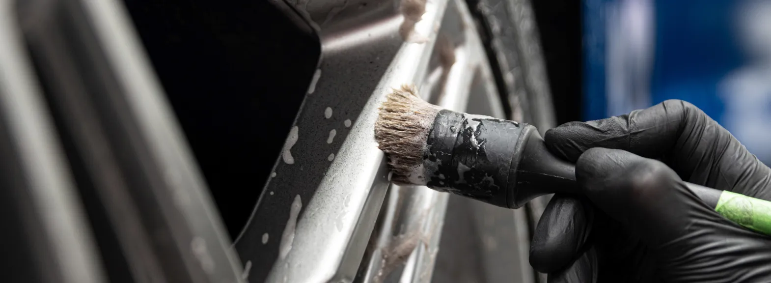 Dettaglio di car detailing: pennello e mano guantata al lavoro su una vettura